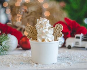 White cup of hot cocoa topped with whipped cream and gingerbread cookies amid festive Christmas decorations.