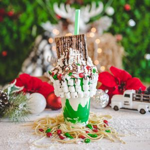 Overloaded Christmas milkshake in green cup with marshmallows, chocolate drizzle, and holiday candy decorations.