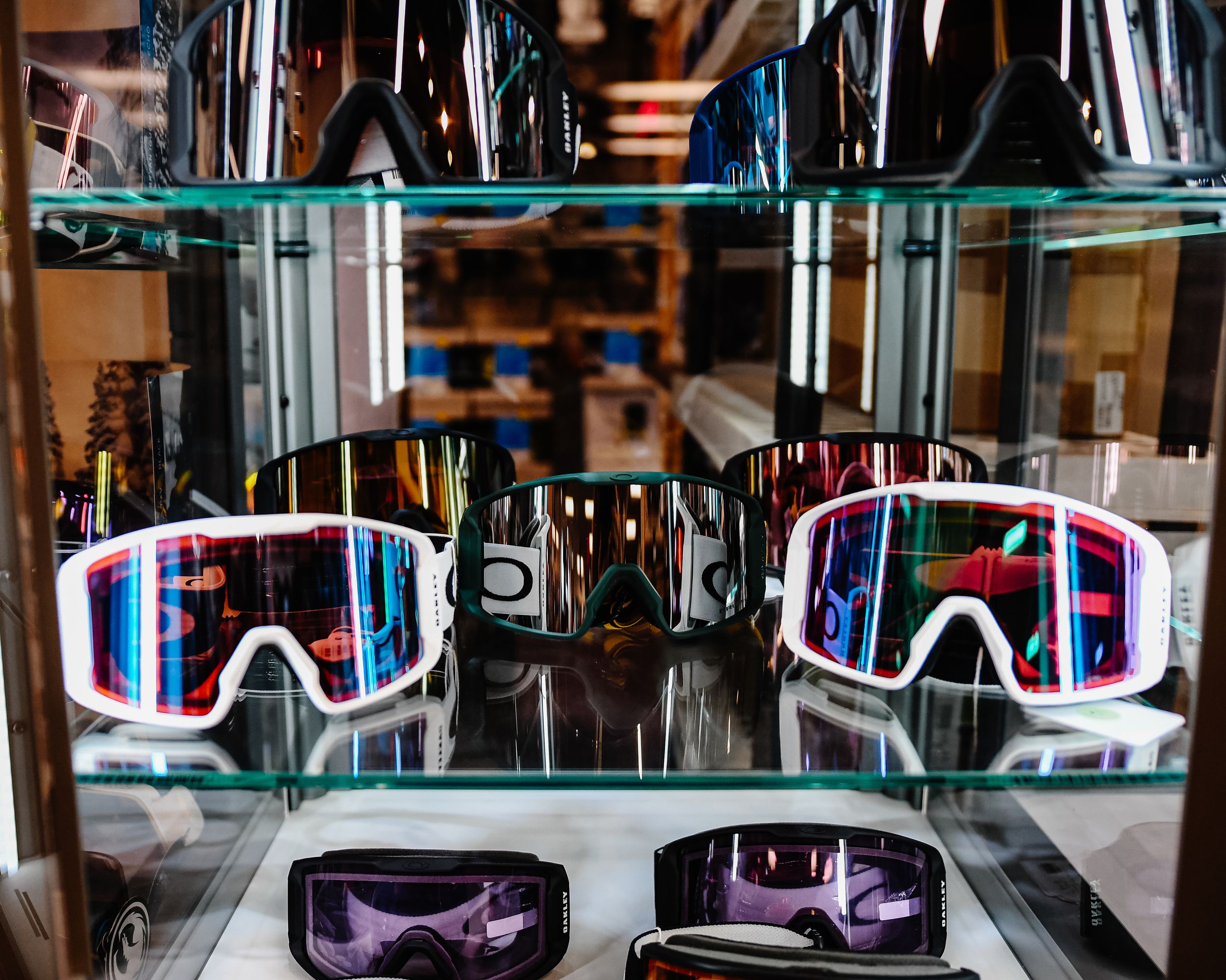 Display case featuring white-framed ski goggles with mirrored lenses on glass shelves in a ski shop.