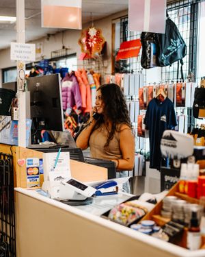 Female retail employee smiling while working at the checkout counter of a ski and outdoor gear shop.