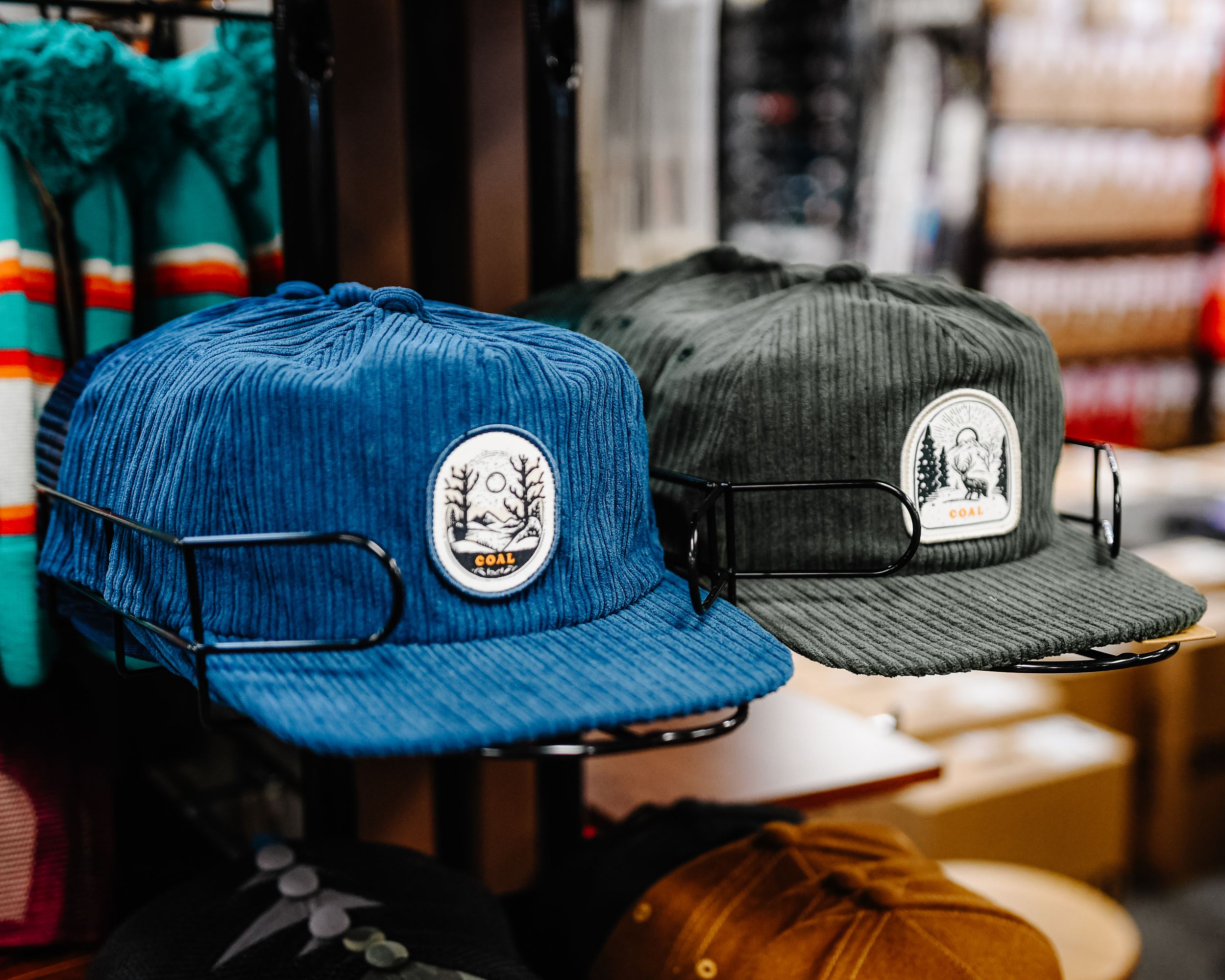 Two corduroy snapback hats with nature patch logos displayed on hat stands in a retail store.