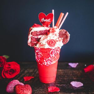 Decadent red velvet freakshake with cookies, whipped cream, sweet heart topper, and sprinkles in a festive red cup.