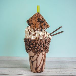 Indulgent chocolate milkshake topped with whipped cream, chocolate chips, brownie, and cookie straws in a drizzled cup.