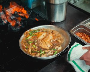 Chicken dish with mushrooms and green onions cooking in a pan beside an open wood fire.