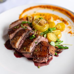 Sliced duck breast with red wine sauce, roasted potatoes, and orange puree on a white plate.