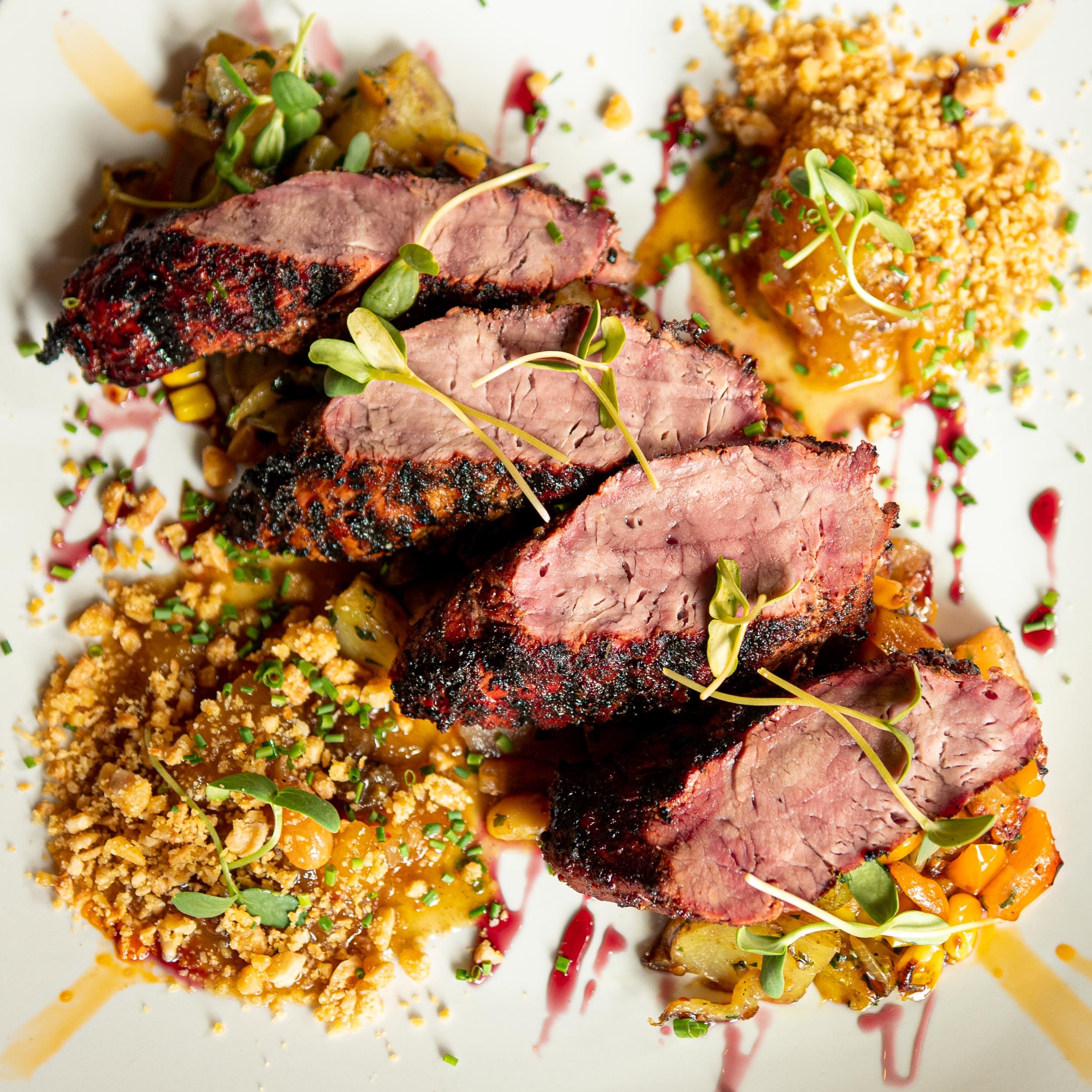 Sliced medium-rare lamb with grain salad, herbs, and pomegranate on a white plate.