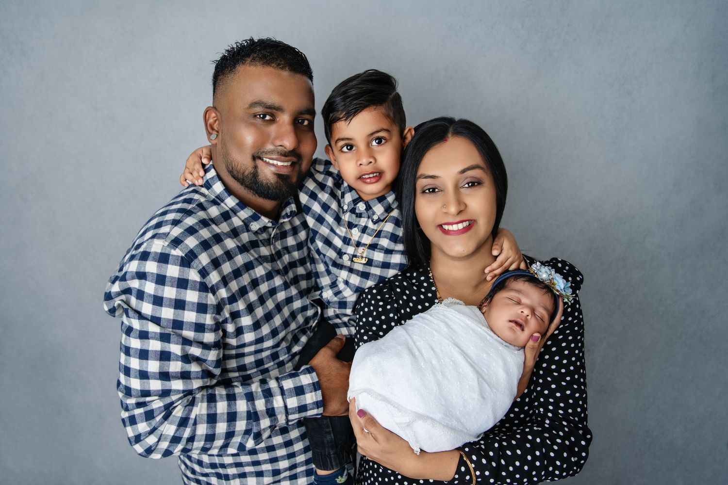 Family in matching blue and white outfits poses against grey studio background.