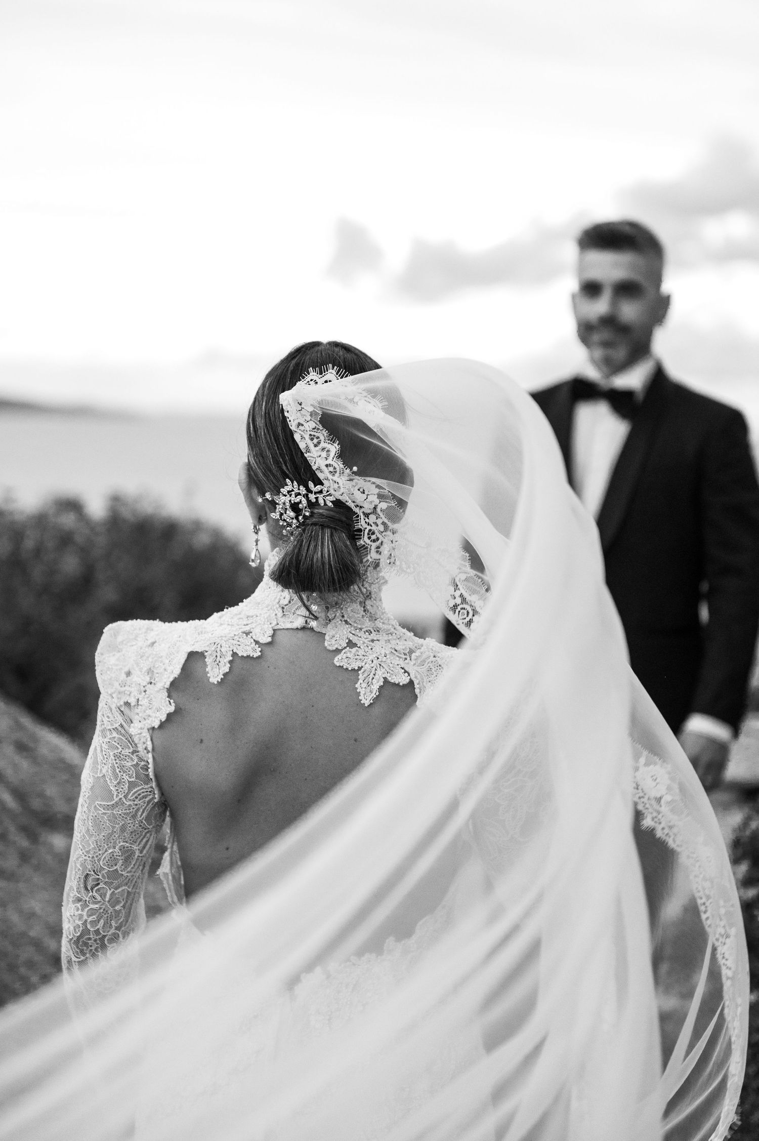 Artistic black and white photo showing bride's backlit veil and lace dress details.