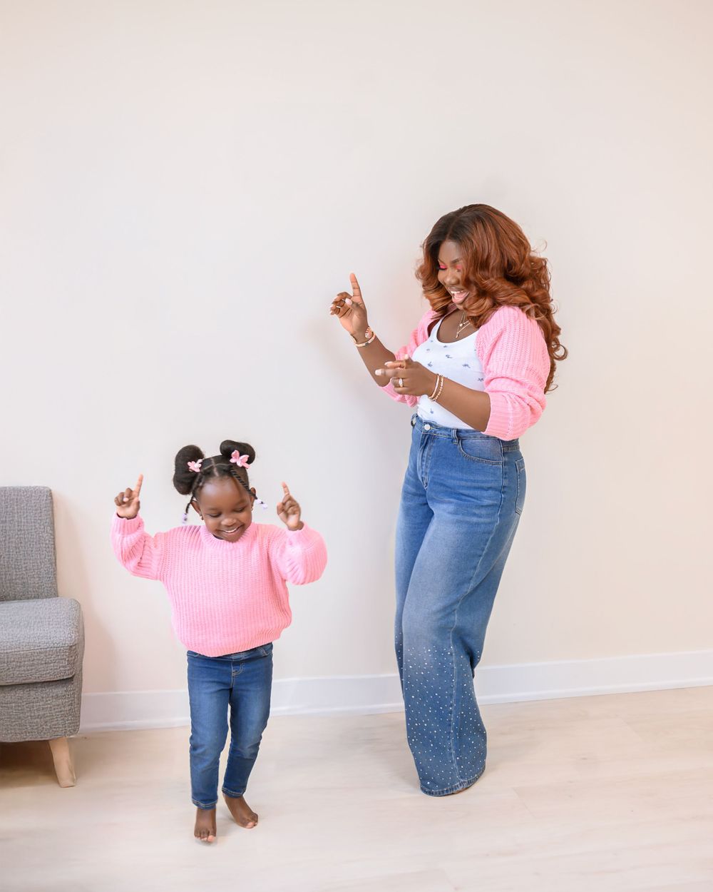 A parent and child wearing matching pink tops and jeans dance together joyfully in a minimalist living room.