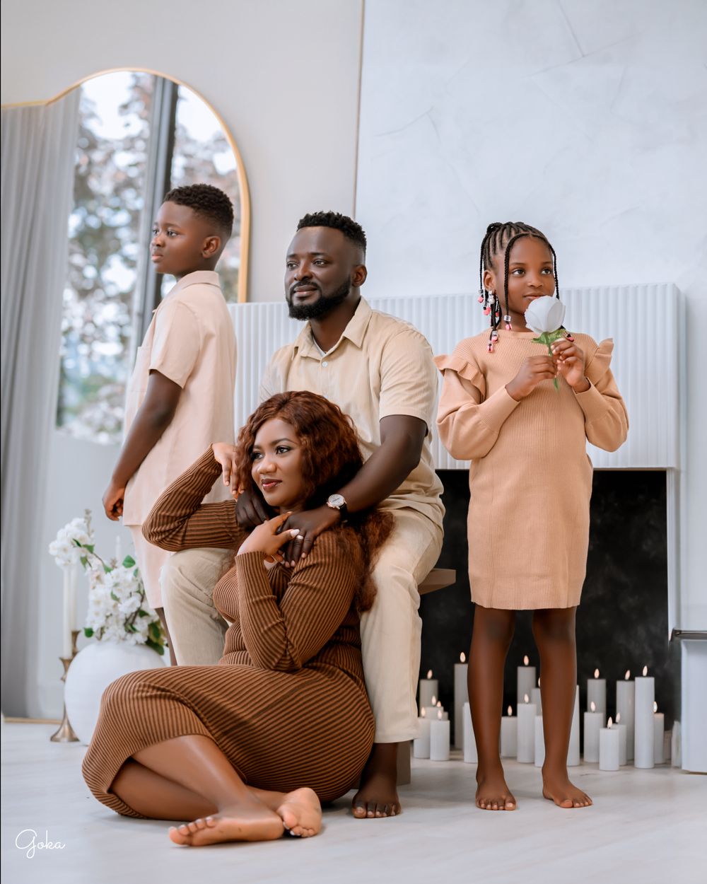 Family wearing coordinated beige and brown outfits poses together in a bright living room interior with mirror.