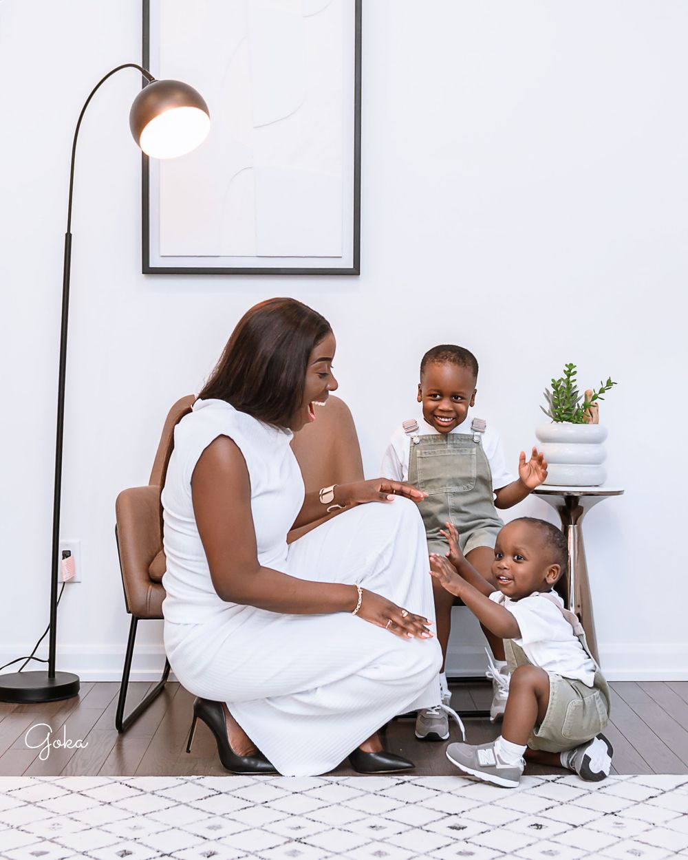 Three people sharing a sweet moment on a patterned rug in a minimalist room with a floor lamp and small plant decor.