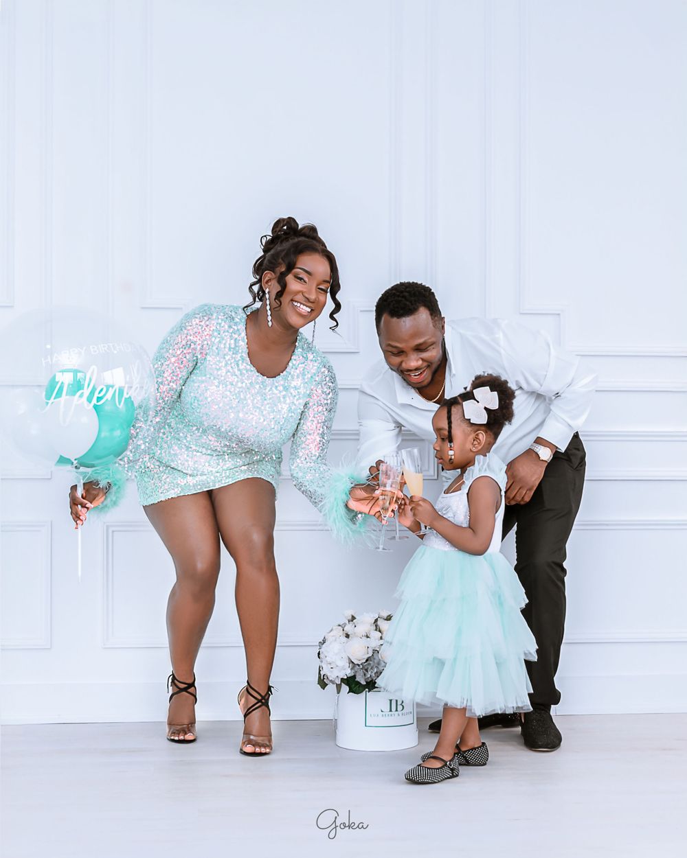 A family wearing matching mint green and white outfits poses playfully against a white backdrop during a photo session.