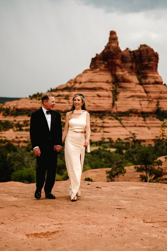 Couple walking on Sedona red rocks with iconic Bell Rock formation in background.