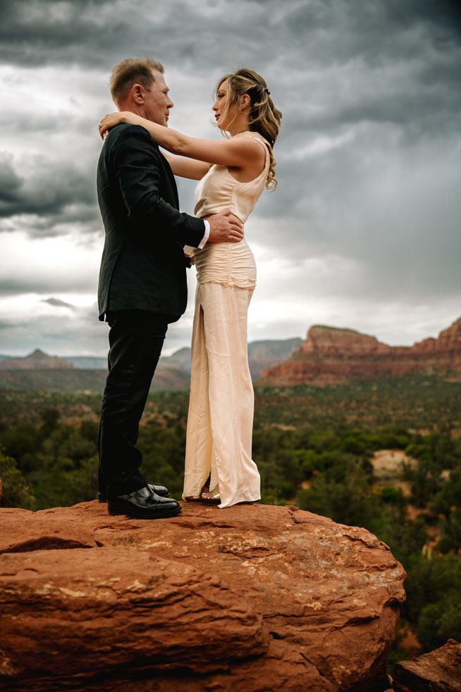 Intimate moment captured on edge of Sedona red rock cliff with dramatic storm clouds.