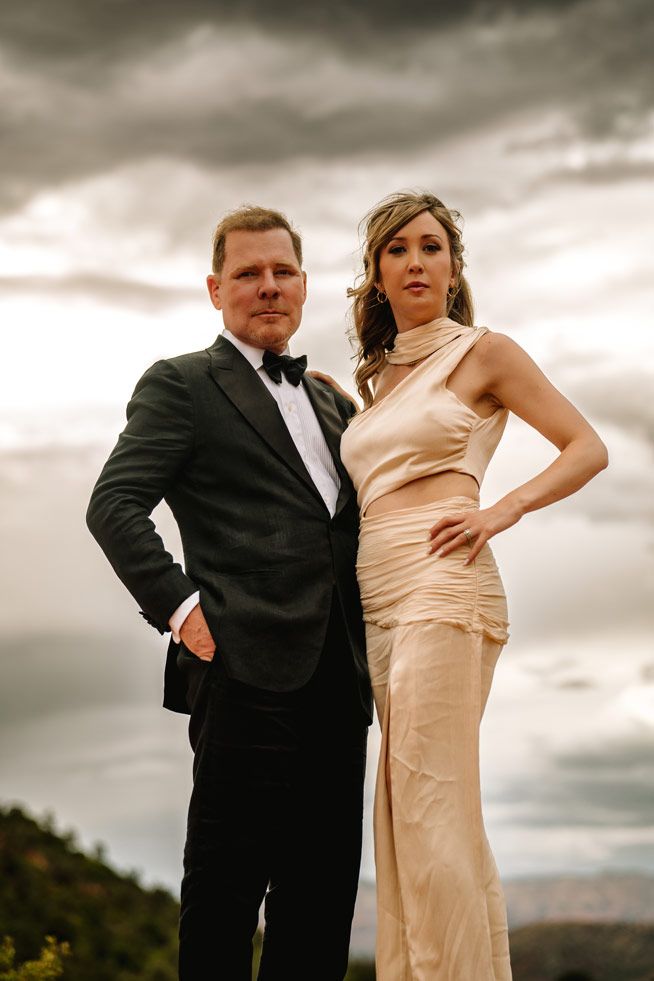 Formal couple poses against stormy Sedona desert sky in elegant attire.