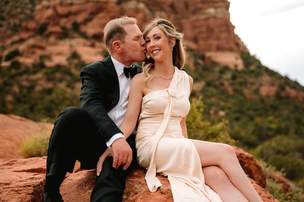 Tender moment shared on Sedona red rocks with desert mountains in background.