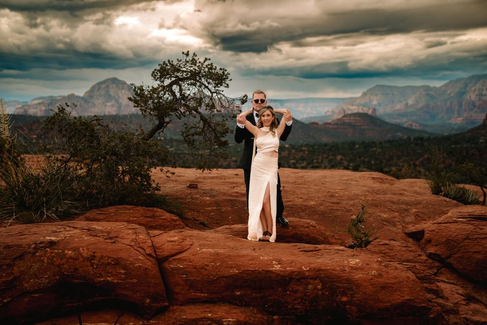 Dramatic wedding portrait on Sedona red rocks with mountain vista and moody sky.