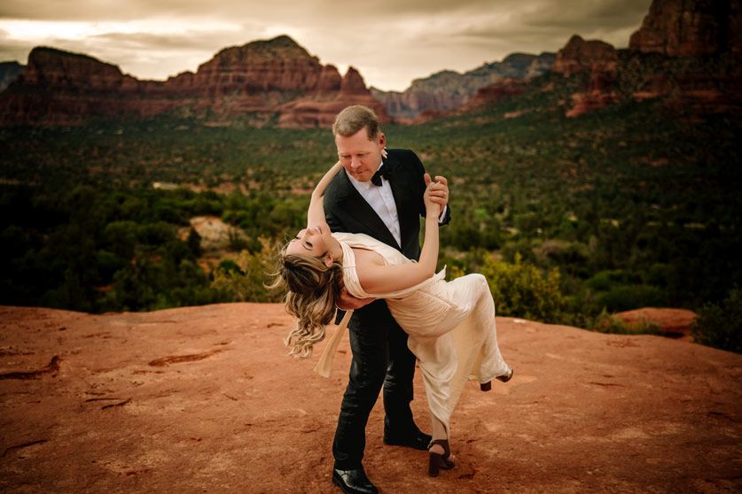 Dramatic dip pose on Sedona red rock overlook with desert valley behind.