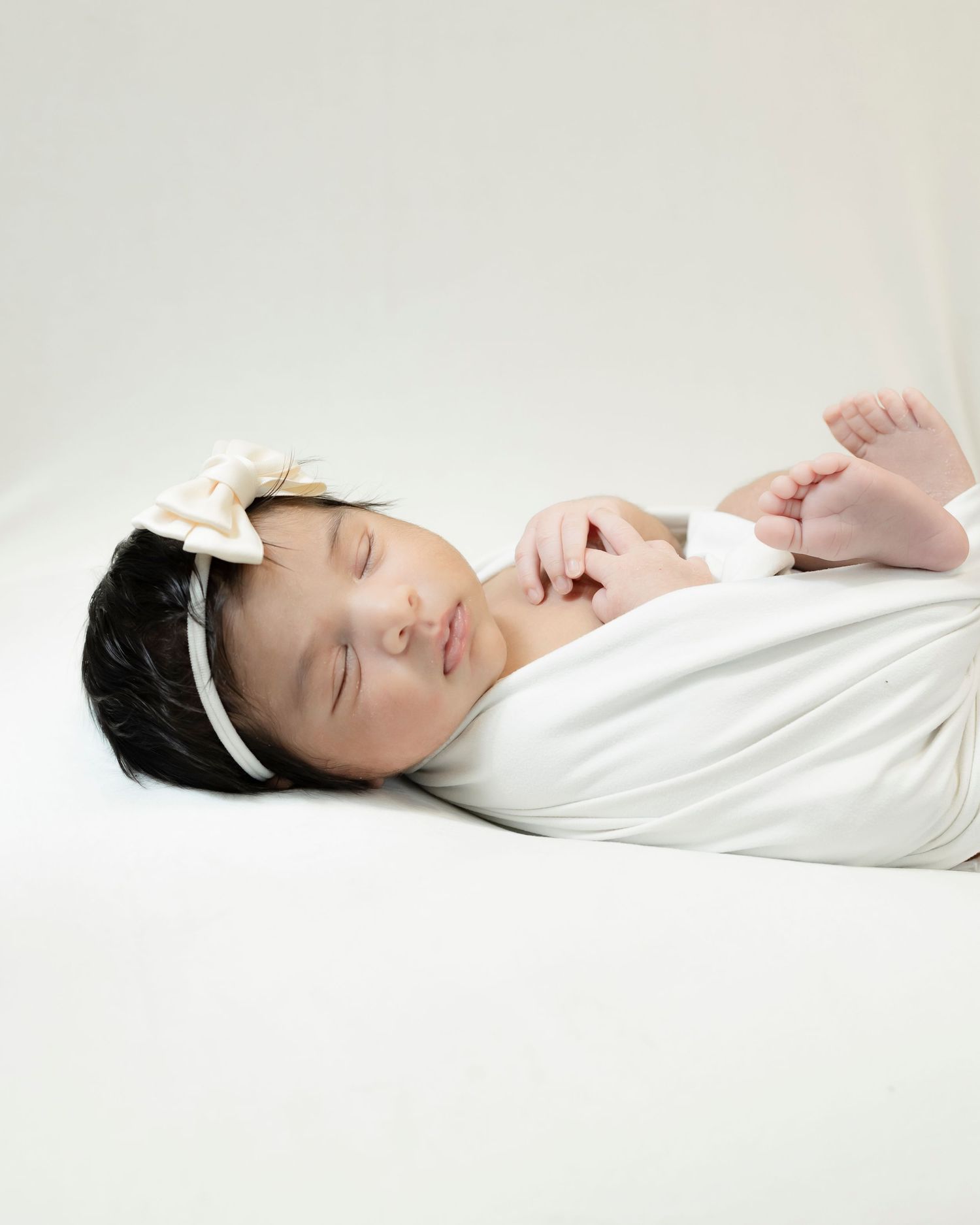 Resting baby with white headband wrapped in soft fabric on neutral background.