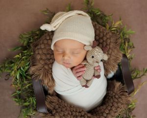 Cozy brown and white newborn photography setup with knit blanket, greenery wreath, and small plush toy.