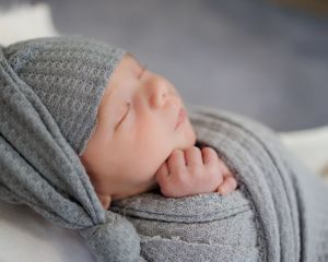 Peaceful sleeping newborn wrapped in soft gray knitted fabric with tiny hand resting near face.
