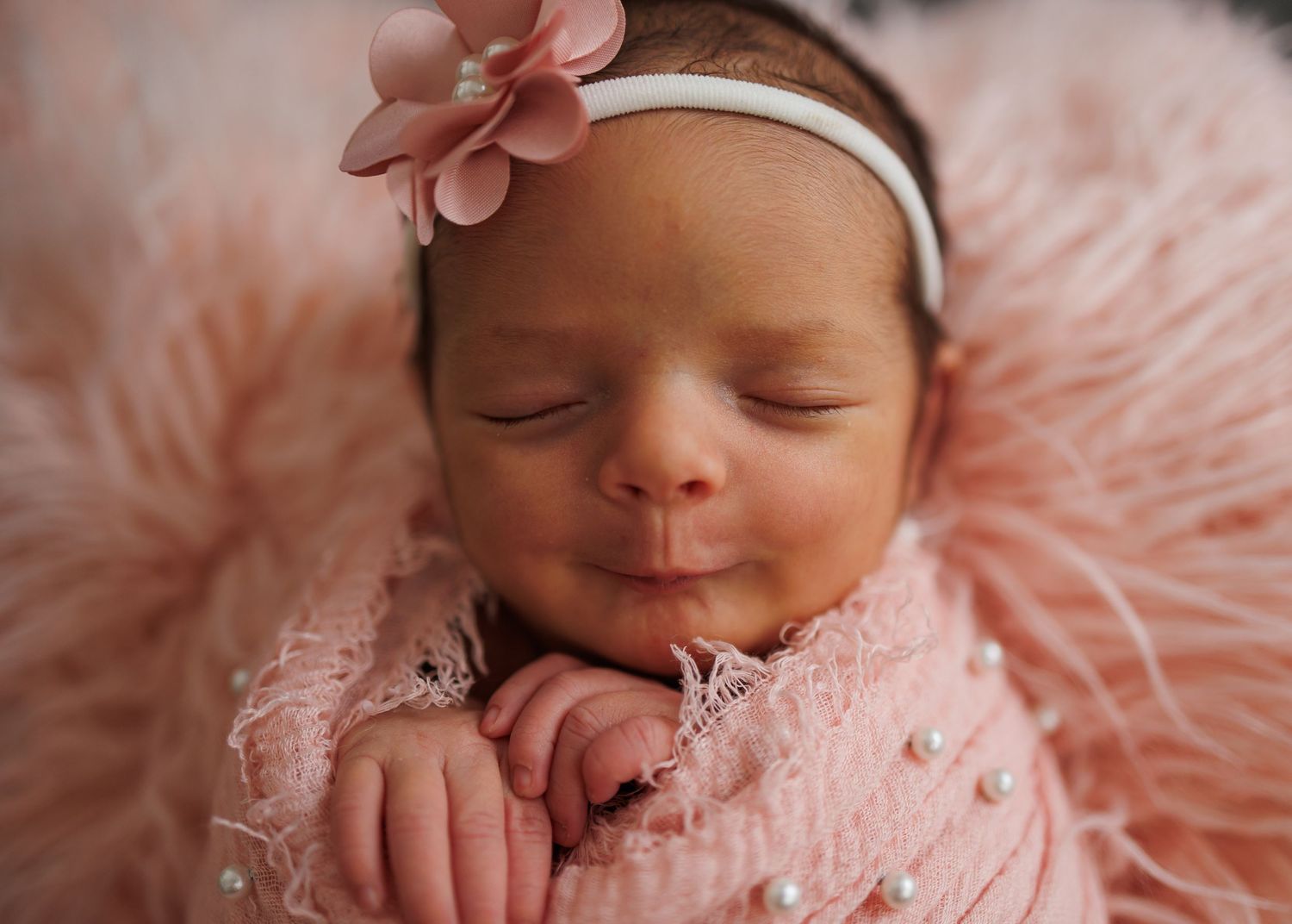 Newborn baby sleeping peacefully in soft pink blanket with delicate lace details.