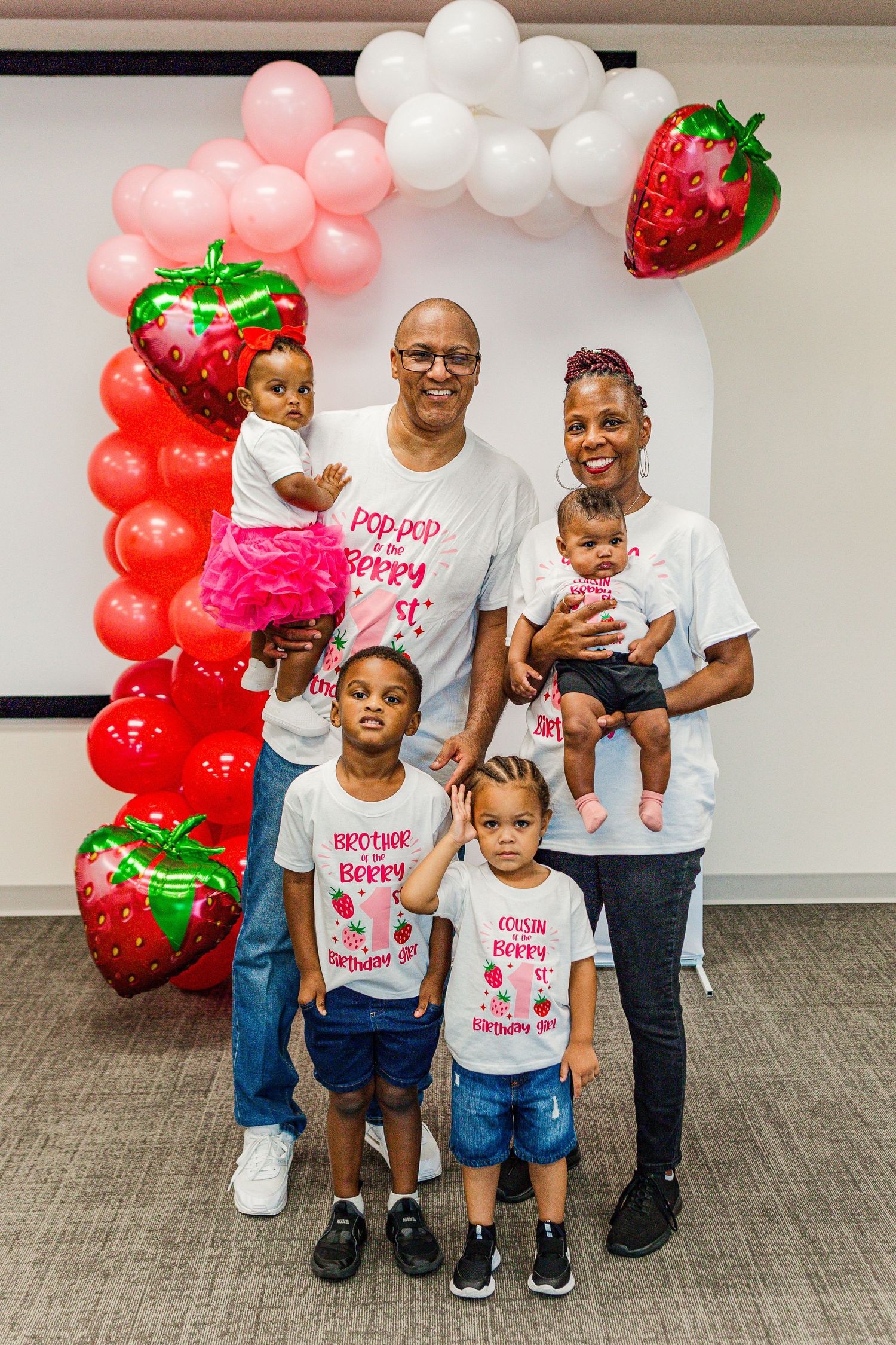 Festive strawberry-themed first birthday party setup with balloon arch and decorations.