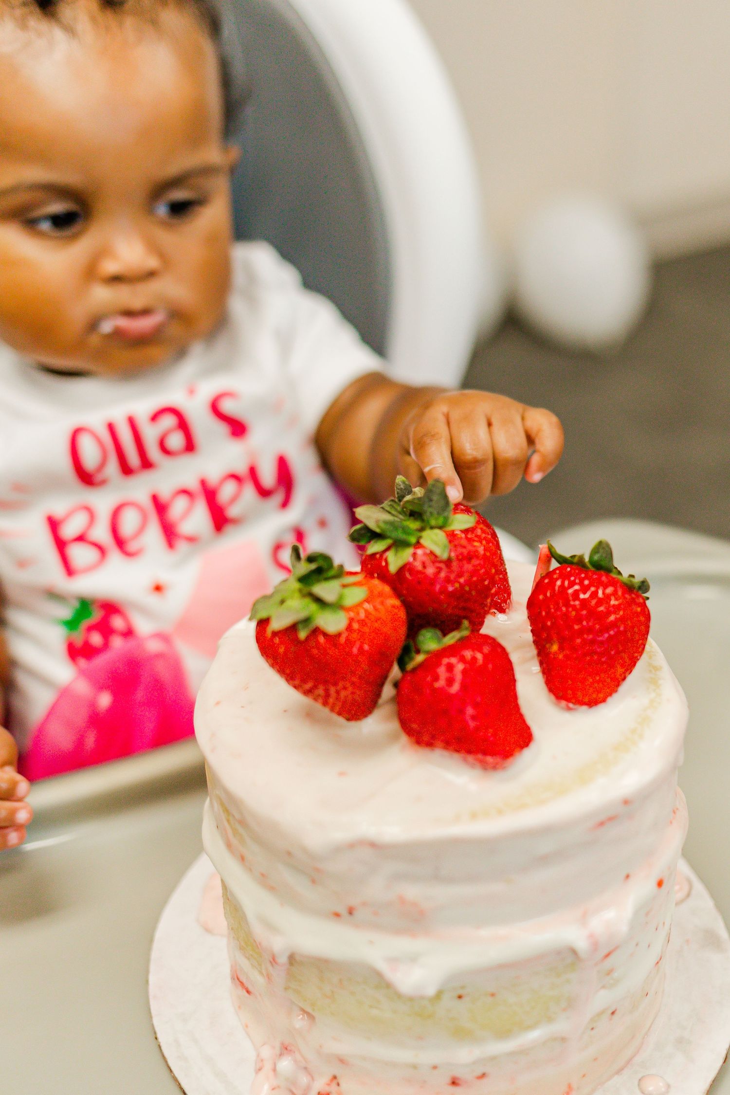 Small hands reaching for fresh strawberries on top of a white frosted cake.