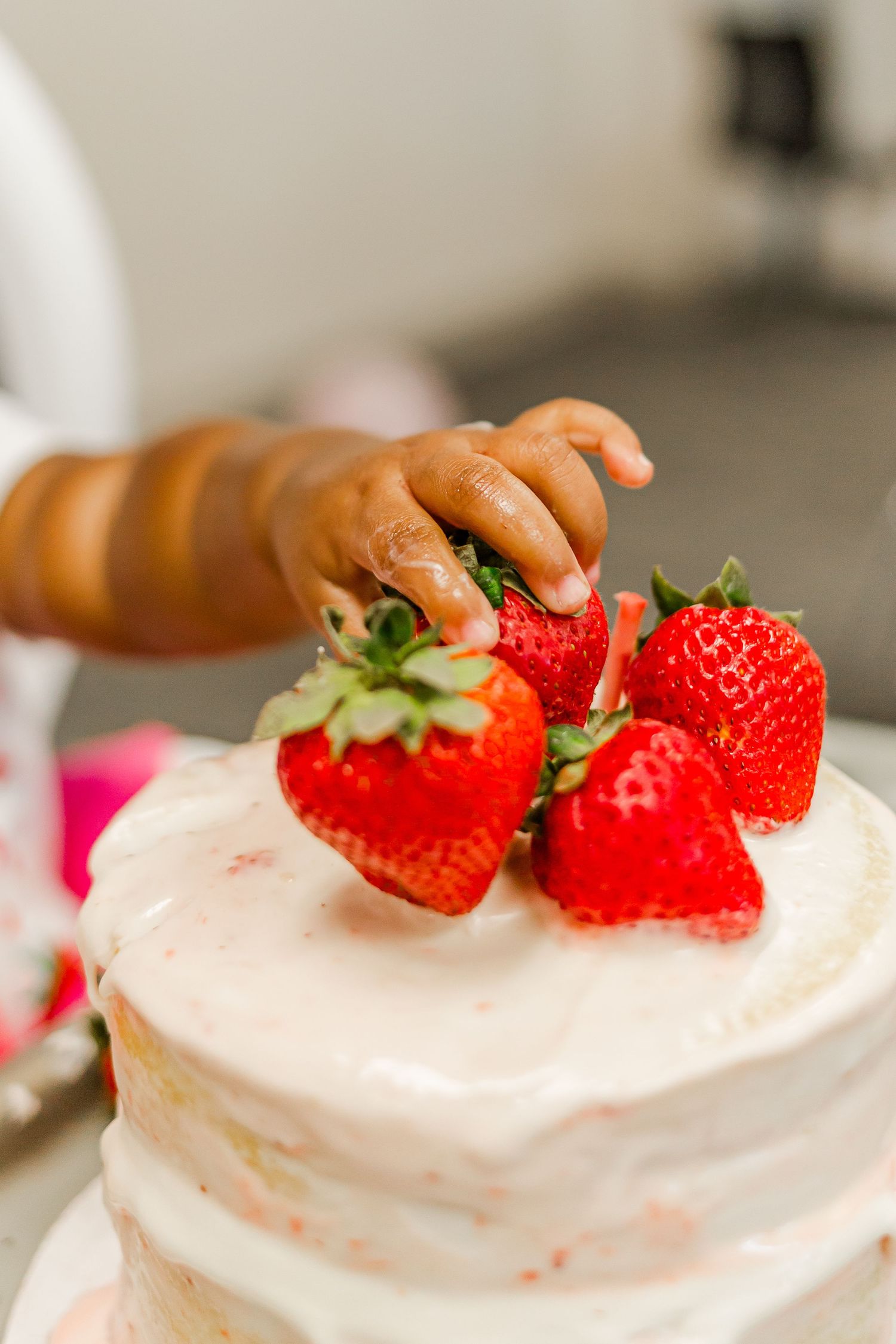 Close-up of hands arranging fresh strawberries on a white frosted layer cake.