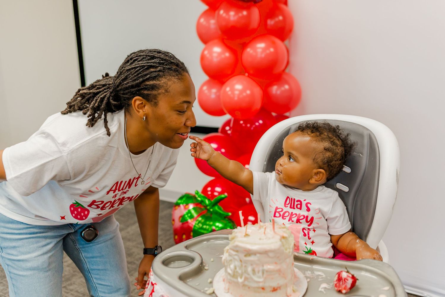 A sweet interaction during a birthday party with red balloon decorations in the background.