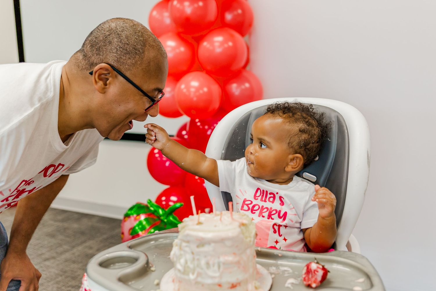 A playful moment shared during a strawberry-themed birthday celebration.
