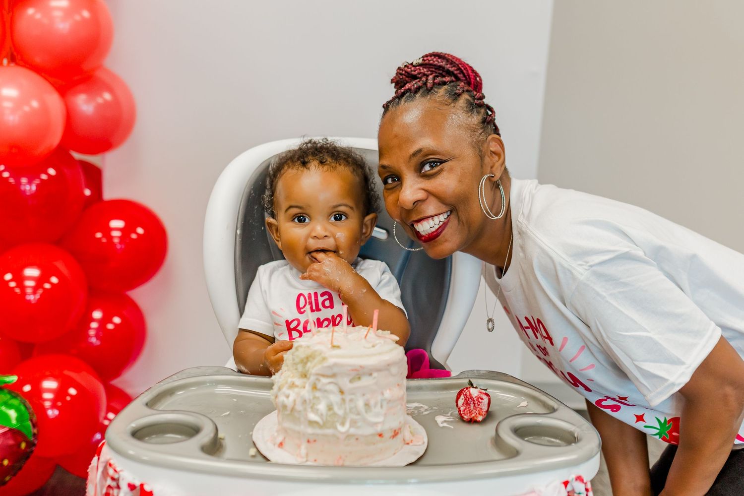 A festive birthday party scene with red balloons and white cake on a high chair.