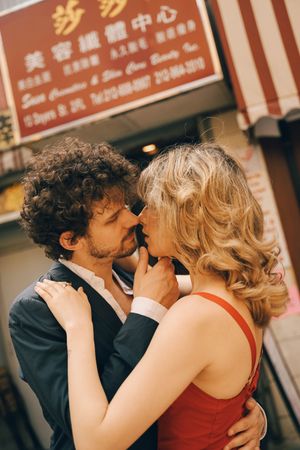 Romantic couple embracing and kissing in front of a Chinese storefront sign in an urban setting.