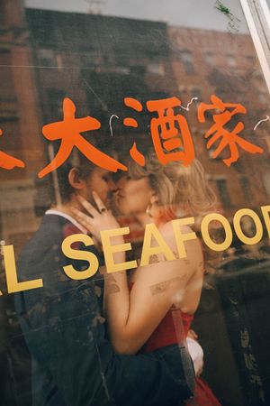 Couple kissing behind a seafood restaurant window with Chinese characters in New York City's Chinatown.
