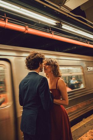 Romantic couple sharing an intimate moment on a NYC subway platform with a blurred train passing behind them.