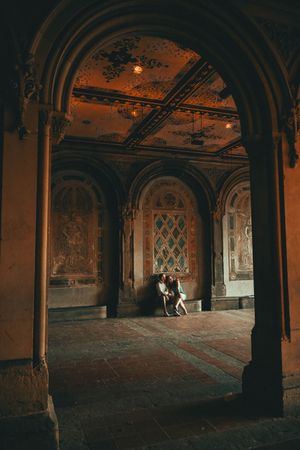 Couple sitting together under ornate arched ceiling with warm amber lighting in historic Bethesda Terrace, Central Park.