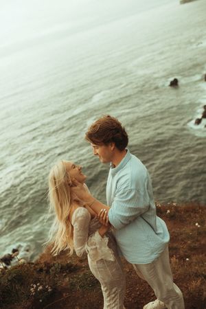 Two people share an intimate moment on a rugged oceanside cliff during golden hour.