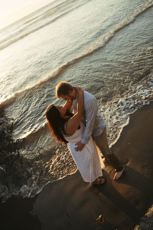 Romantic couple shares intimate moment on sandy beach shore during golden hour.