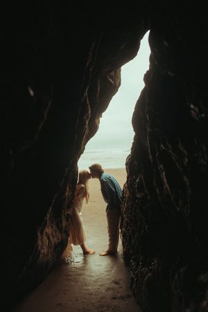 A silhouette of a figure explores a dark cave tunnel with sunlit beach visible through the opening.