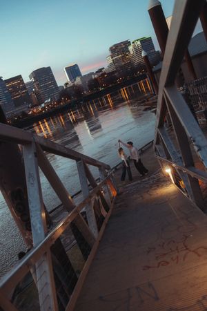 People enjoying sunset views along a waterfront pier with city skyline silhouetted in the background during dusk.