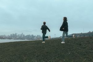 Two people running on a hilltop overlooking a city skyline on an overcast day.