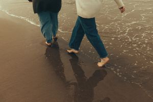 People walking barefoot on wet sand at the beach during sunset creating long shadows on the shore.