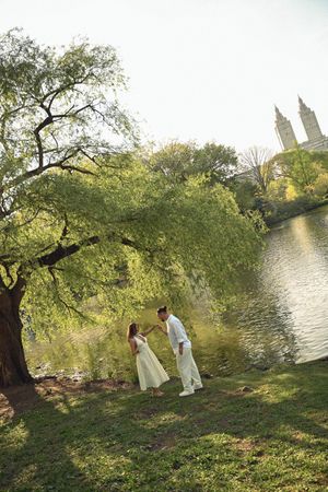Couple in white attire standing under a willow tree by a lake in Central Park, NYC.