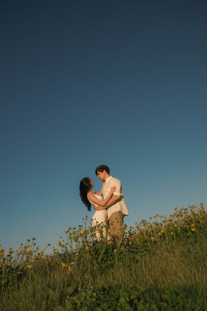 Couple embracing romantically in a wildflower meadow under a clear blue sky at golden hour.