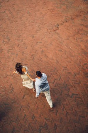 Aerial view of a couple dancing on a herringbone brick patio, woman in white dress and man in light blue suit.