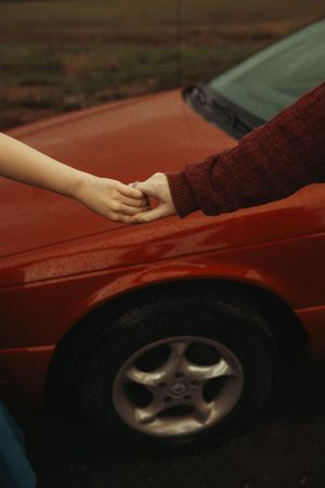A hand slides across the surface of a red car's hood, demonstrating paint damage and scratches.
