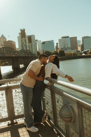 Couple embraces while looking out over the river with city skyline in background on sunny afternoon.