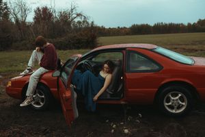 A sequence of photos showing someone lying down next to a red sports car in a rural field at dusk.