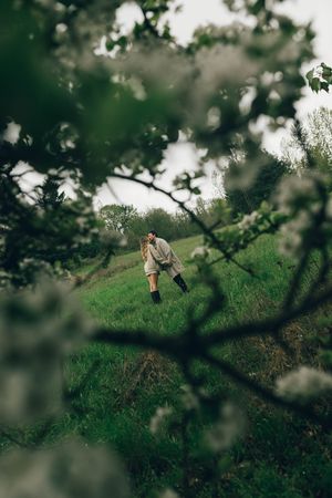 Person standing on a lush green hillside framed by blossoming tree branches in a serene countryside landscape.