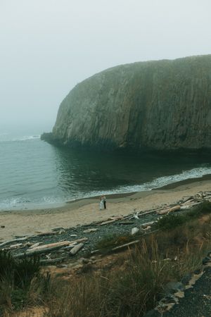 Dramatic coastal landscape with steep cliffs and rocky beach along misty shoreline on an overcast day.